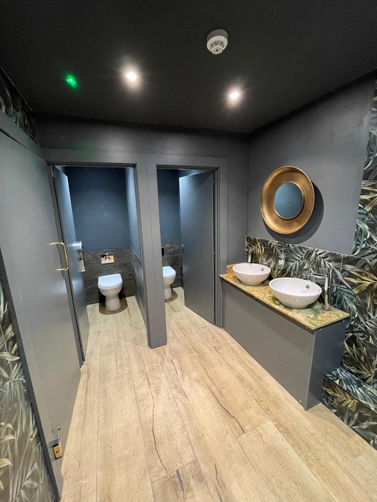 Customer toilets with tropical wallpaper and brass mirror