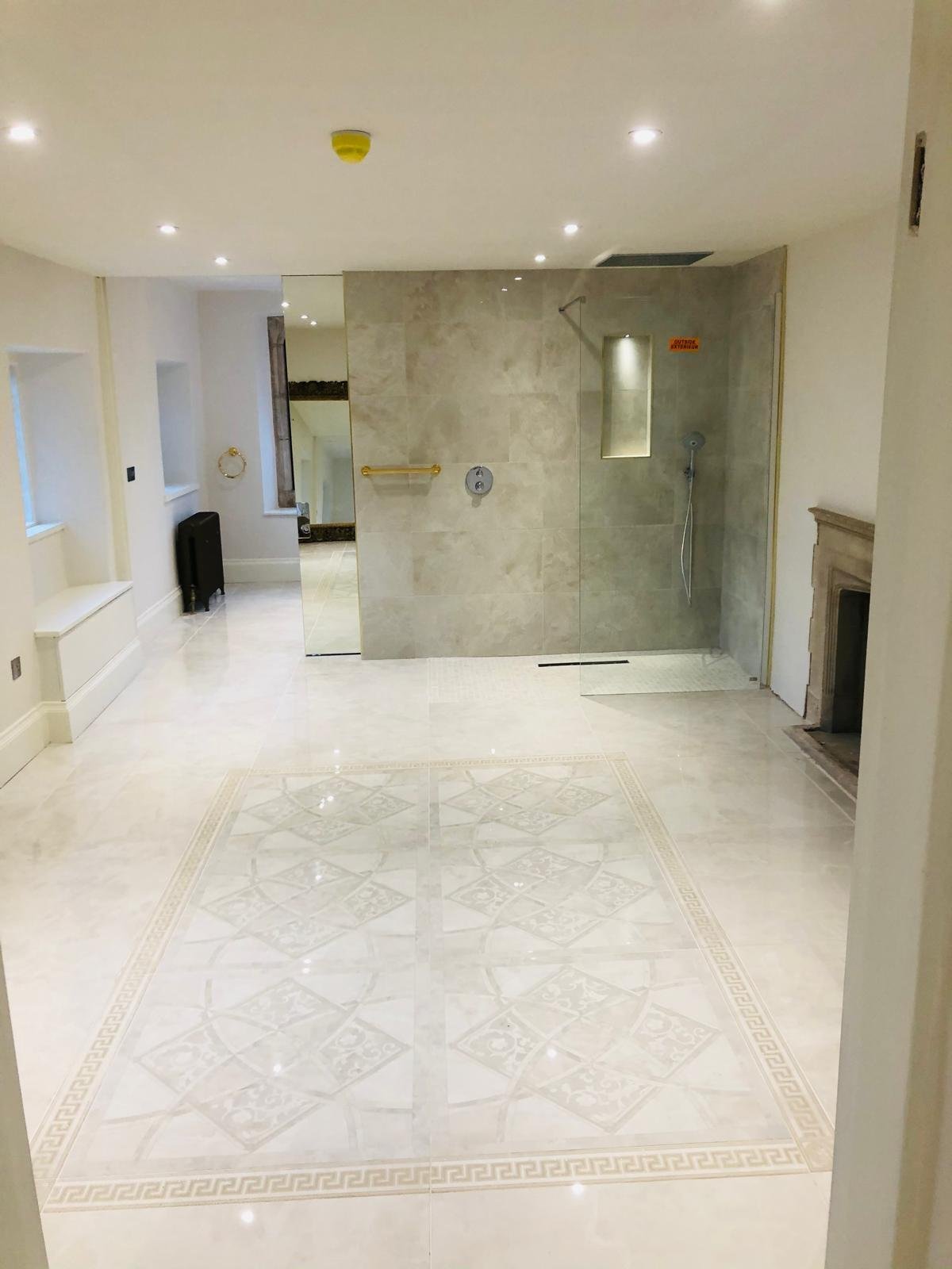 Luxury walk-in shower bathroom with patterned marble floor and stone fireplace in Oxfordshire